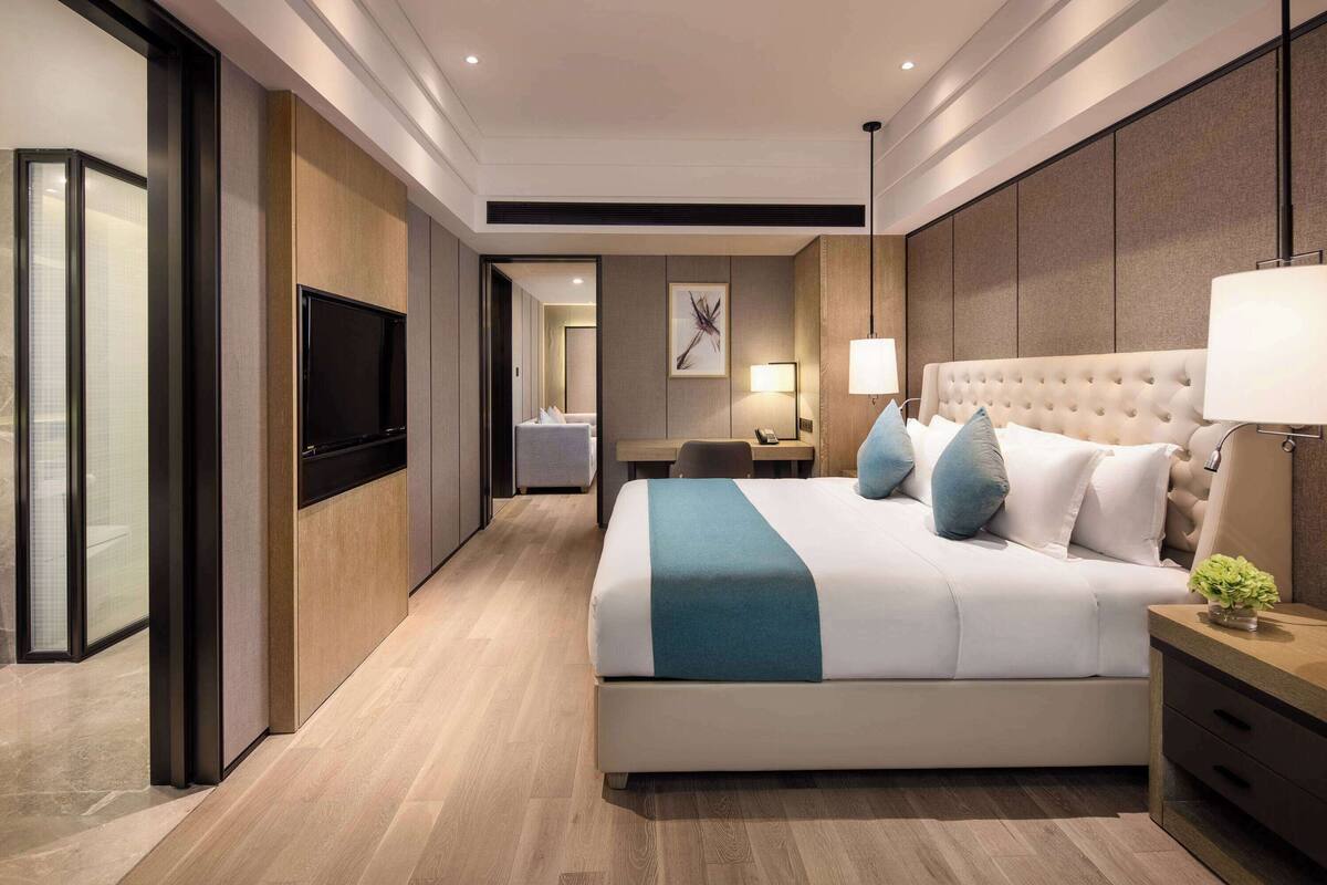 A modern hotel room with a large bed, a flat-screen TV, a desk, and a nightstand.