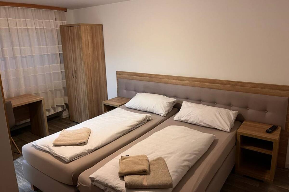 A hotel room with two beds, a wooden wardrobe, a small table, and a nightstand.