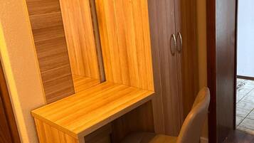Une petite pièce comprenant un bureau en bois intégré, une chaise, une armoire avec un miroir et un panneau vert sur le mur.
