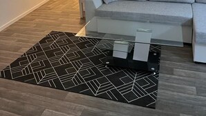 A modern living room with a grey sofa, a black and white rug, and a glass coffee table. - Hotel zur Post (Hünfelden)