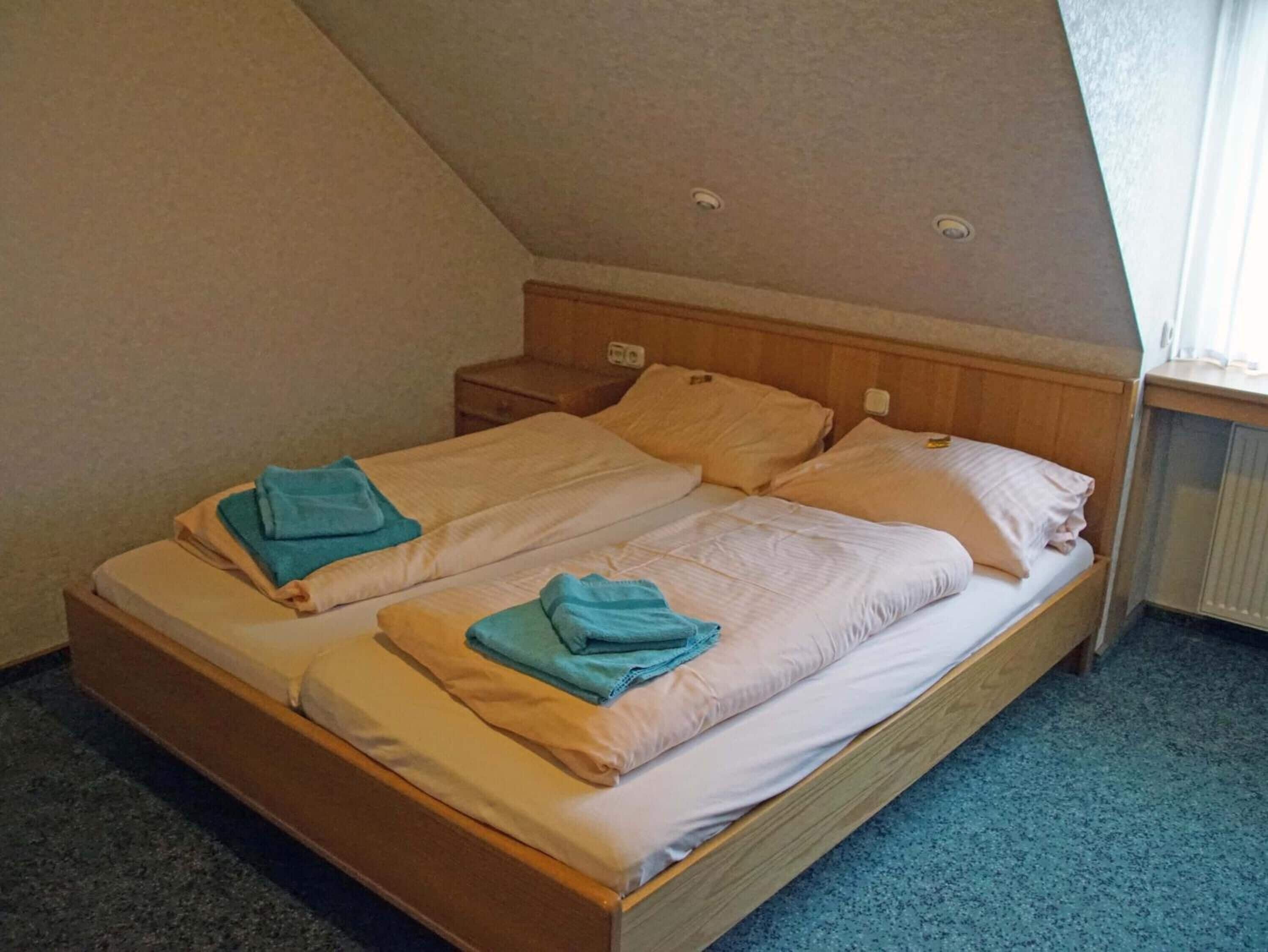Una cama individual con cabecera de madera, dos mesitas de noche y una ventana con vistas al exterior.