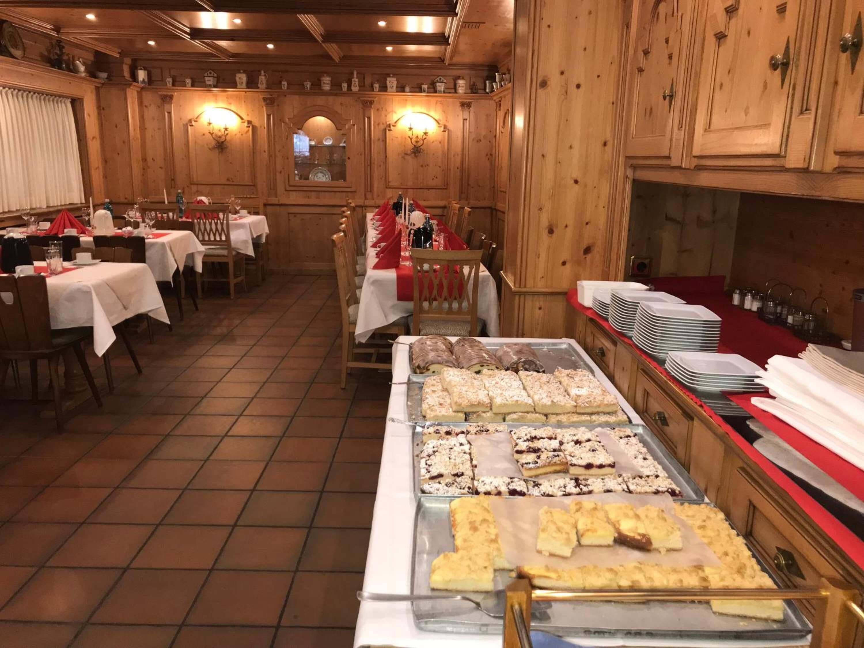 Un restaurante con interiores de madera, varias mesas con manteles blancos y un bufé con diversas opciones de panadería.