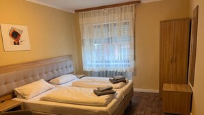 A bedroom with a large bed, a wooden wardrobe, and a window with sheer curtains. - Hotel zur Post (Hünfelden)