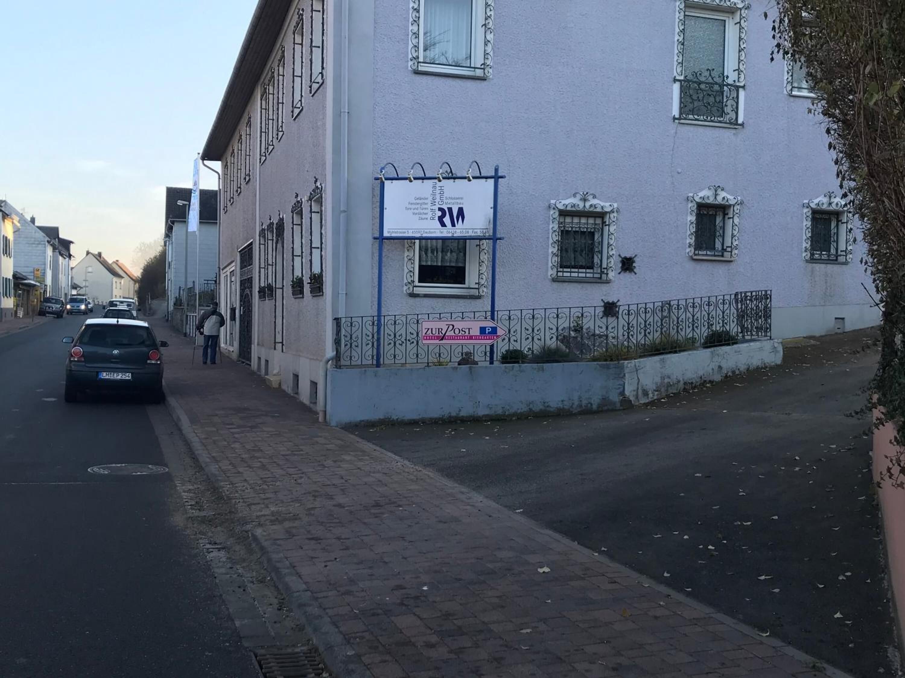 A building with a sign for 'Zur Post Restaurant' and a parking sign.