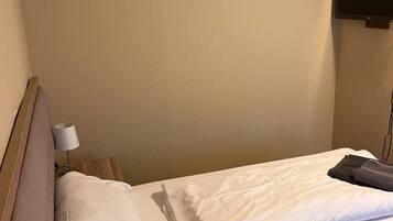 Ein Hotelzimmer mit einem Einzelbett, einem Nachttisch mit Lampe und einem an der Wand befestigten Fernseher.