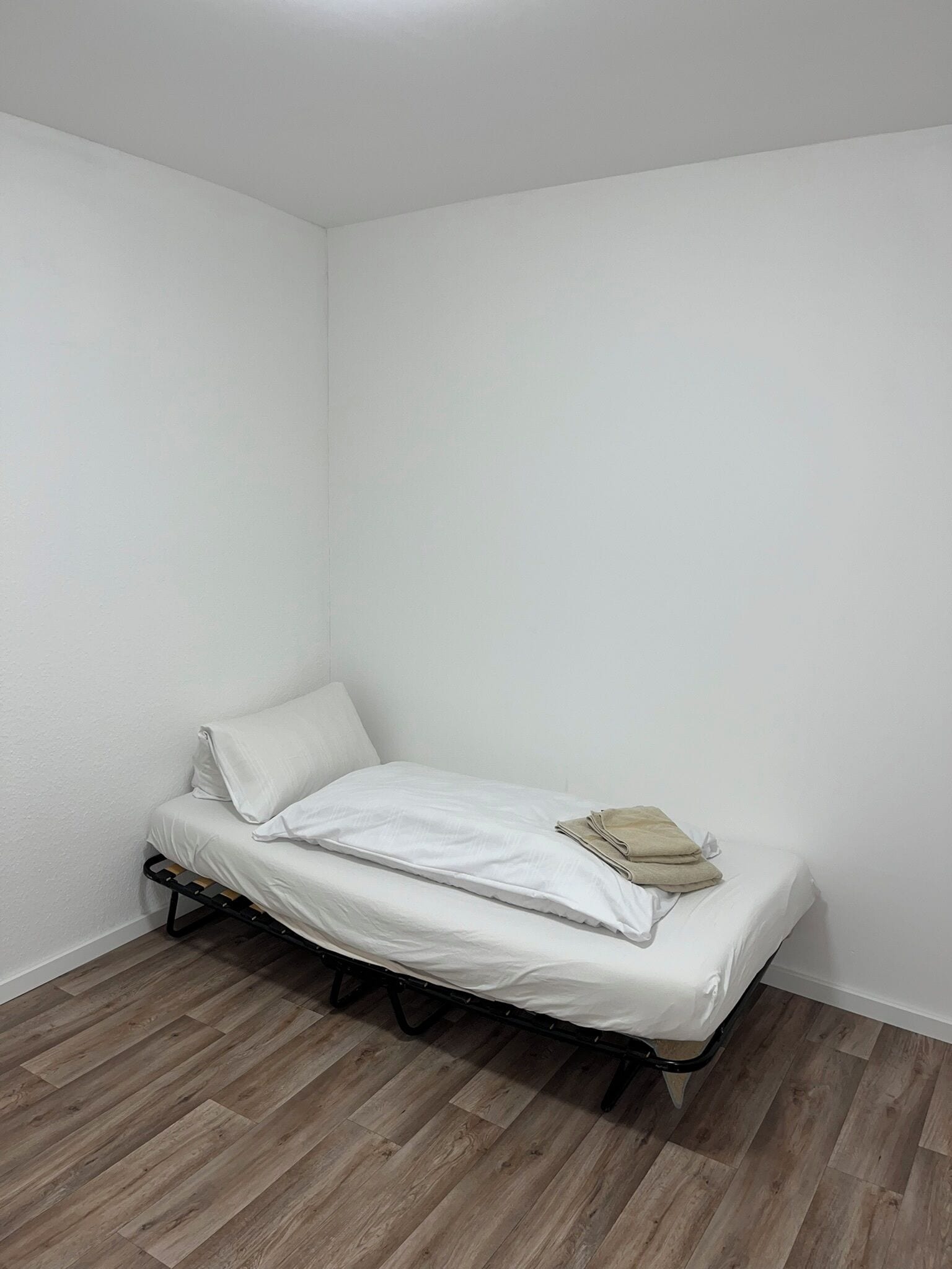 A small, single-bed room with a wooden floor and white walls.