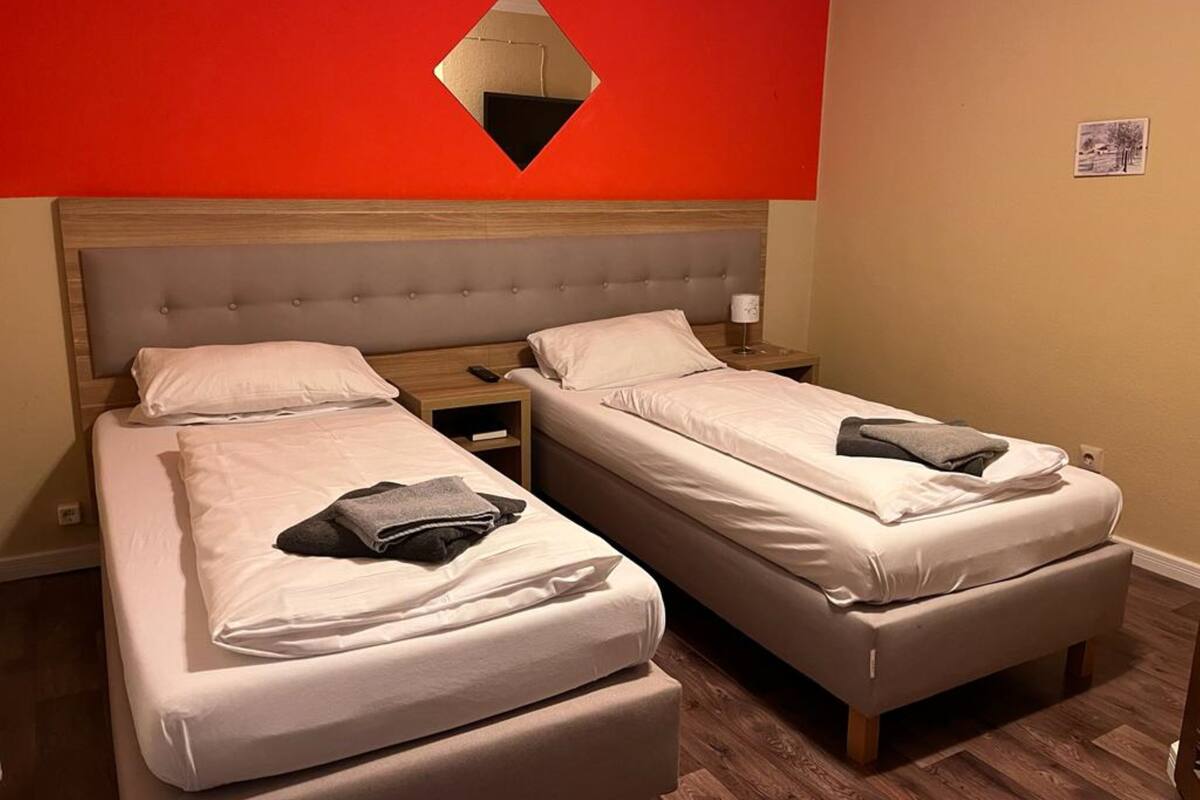 A hotel room with two single beds, a wooden headboard, a red accent wall, and a small mirror.
