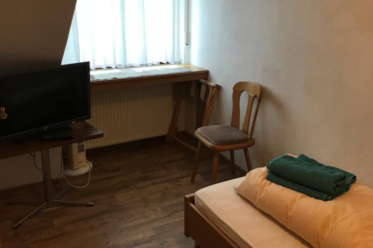 A bedroom with a bed, a chair, a TV, and a window with curtains.