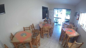 A dining area with multiple wooden tables and chairs, a refrigerator, and a fire extinguisher. - Pousada Cordeiro (Penha)