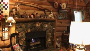 Een gezellig blokhutinterieur met een stenen open haard, houten wanden, een schommelstoel en een geborduurde wanddecoratie.