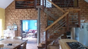 Eine rustikale Küche mit Backsteinwand, einer Holztreppe und einem Essbereich mit Tisch und Stühlen.