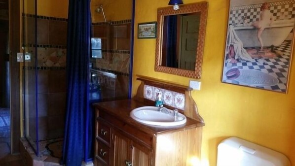 A bathroom with a wooden vanity, a sink, and a mirror. There is a shower area with a glass door and a blue curtain.