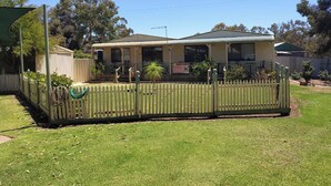 A single-story house with a covered porch, a fenced yard, and a sign indicating a business. - Riverside Golf Club 3 Bedroom Holiday House (Nichols Point)