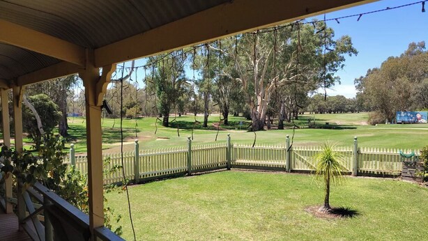 A covered outdoor area with a wooden deck, a fenced lawn, and trees in the background. - Riverside Golf Club 3 Bedroom Holiday House (Nichols Point)