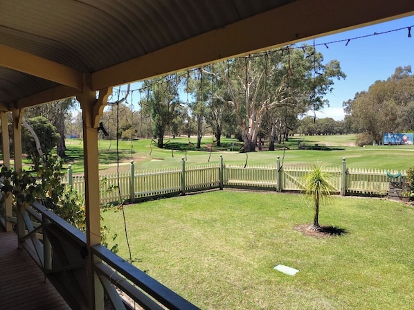 A covered outdoor area with a wooden deck, a fenced lawn, and trees in the background.