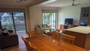 A spacious living area with a wooden dining table, a sofa, and a television. - Riverside Golf Club 3 Bedroom Holiday House (Nichols Point)