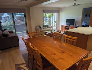 A spacious living area with a wooden dining table, a sofa, and a television.