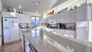 Una cocina moderna con armarios blancos, encimera de granito y electrodomésticos varios, incluyendo un refrigerador, microondas y estufa.
