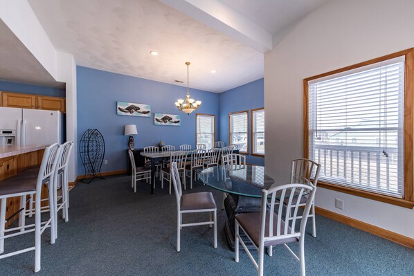 A dining area with a glass table surrounded by white chairs, a chandelier, and artwork on the walls.