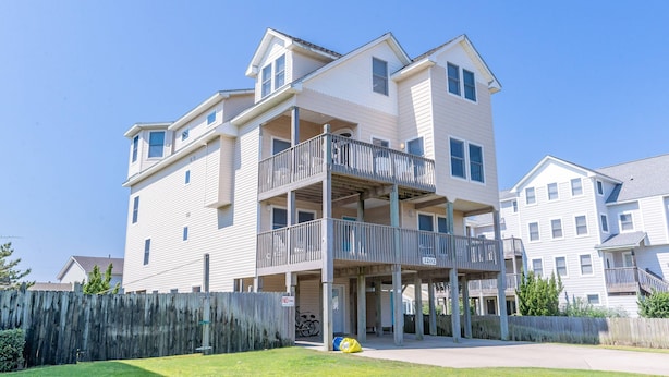 A multi-story residential building with balconies, a wooden fence, and a clear sky. - Cloud Nine - KDH MP 7, Semi-Oceanfront, Ocean View, 120 Yds to Beach, Pool, Hot Tub, Pets OK (Kill Devil Hills)