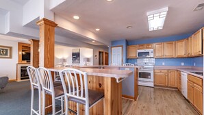 A modern kitchen with wooden cabinets, a central island with bar stools, and built-in appliances. - Cloud Nine - KDH MP 7, Semi-Oceanfront, Ocean View, 120 Yds to Beach, Pool, Hot Tub, Pets OK (Kill Devil Hills)