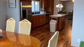 A spacious kitchen with wooden cabinets, a central island, and a dining area with a round table and chairs. - Escape To The Country In Comfort And Style In An Eco-Friendly House (Rushville)