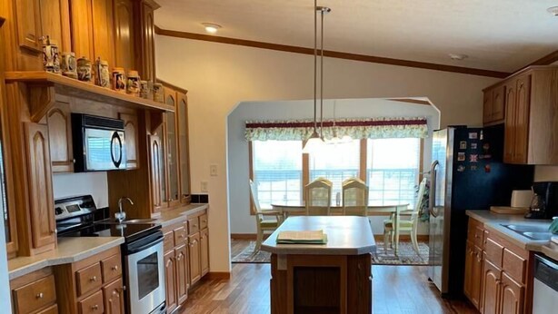 A spacious kitchen with wooden cabinets, a central island, and a dining area with a view. - Escape To The Country In Comfort And Style In An Eco-Friendly House (Rushville)