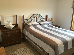 Una cama bien tendida con ropa de cama a rayas, una mesita de noche de madera con una lámpara y una jarra decorativa sobre la mesita.