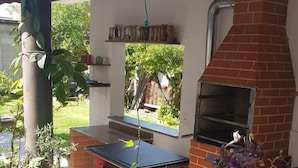 Angolo cucina all'aperto con forno a mattoni, un tavolo e diverse piante in vaso.