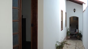 Un cortile stretto con lastre di pietra, un muro bianco, una porta in legno e un piccolo arco che conduce a un ingresso coperto.