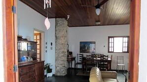 Un'ampia zona giorno con un pilastro in pietra, soffitto in legno, un tavolo da pranzo con sedie e un divano in pelle.