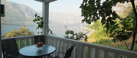 A covered balcony with a table and chairs, overlooking a lake and mountains.