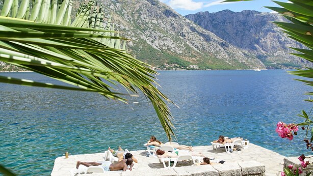 A poolside area with lounge chairs and a view of a lake and mountains.