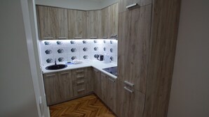 A compact kitchen with wooden cabinets, a white countertop, and a herringbone-patterned backsplash.
