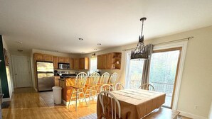 Une cuisine spacieuse avec des meubles en bois, un coin repas comprenant une table et des chaises, et une grande fenêtre laissant entrer la lumière naturelle.