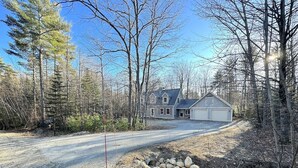 Une maison à deux étages avec un garage, entourée d’une zone boisée.