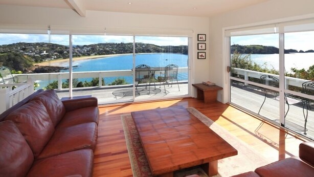 Amplia sala de estar con un gran ventanal corredizo que da a un balc ón con vista a un lago y una playa.