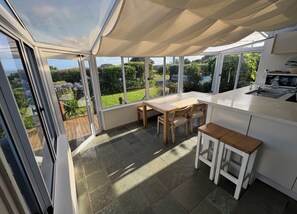 A conservatory with a table and chairs, a sink, and a view of the garden. - Gorgeous beach house on Oneroa Bay (Little Oneroa)