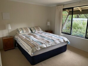 A bedroom with a bed, two bedside tables, a window with curtains, and a view of greenery outside. - Yallingup Hidden Valley (Yallingup)