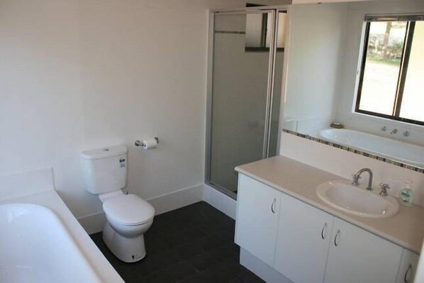 Een badkamer met toilet, douchecabine, wastafel en bad.