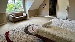 Une chambre avec un plafond en pente, une grande fenêtre, un canapé, un lit recouvert d’une courtepointe à motifs et une armoire.