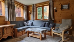 Ein gemütliches Blockhaus-Interieur mit Holzausstattung, einer Couch, einem Sessel, einem Tisch und einem Fenster mit Vorhängen.
