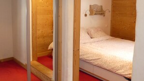 Ein Zimmer mit schrägverdeckter Decke aus Holz, einem Bett mit blumigem Überwurf, einem roten Teppich und einem Spiegel an der Wand.