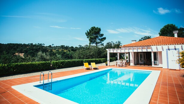 Una piscina con dos sillas reclinables amarillas, un porche cubierto y vistas del paisaje circundante.