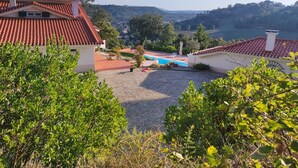 Una villa con techo de tejas rojas, piscina y vistas a las colinas circundantes.