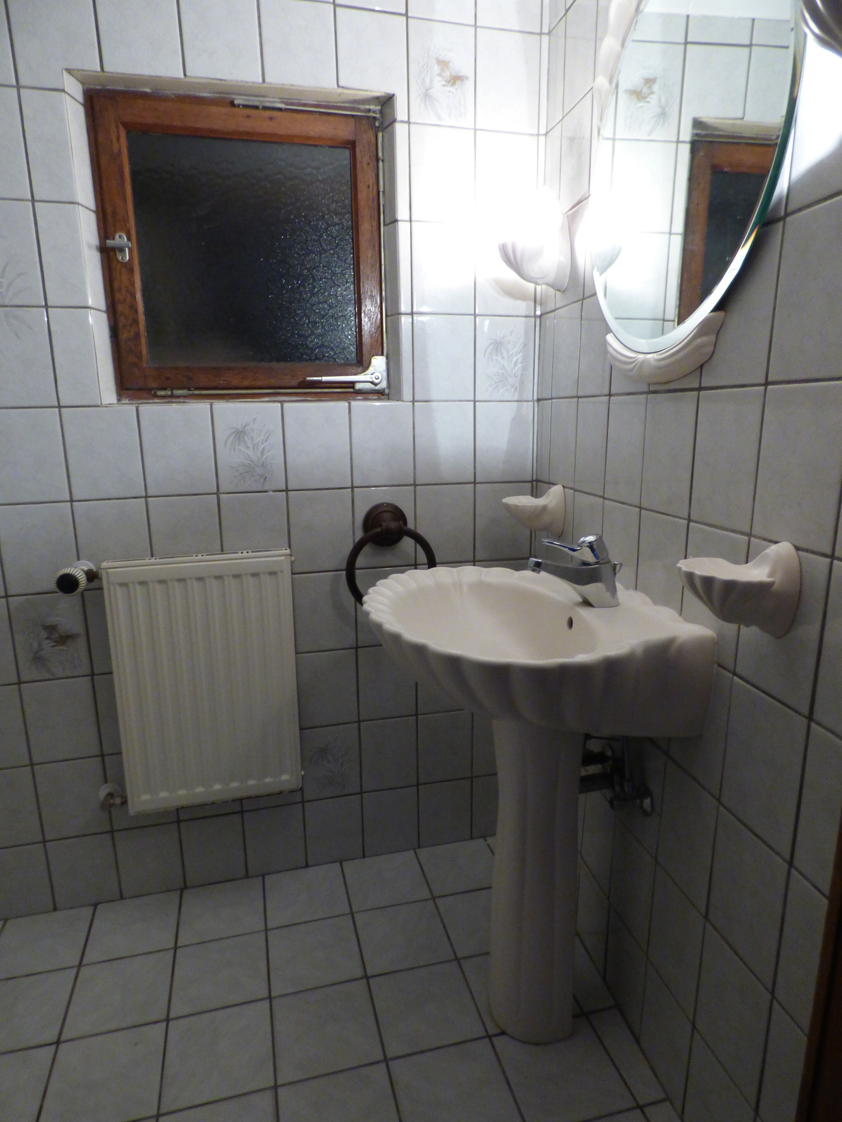 A bathroom with a white sink, a mirror, a window, and a radiator.