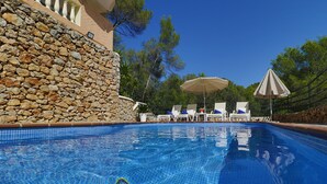 A swimming pool with tiled edges, lounge chairs, and umbrellas.