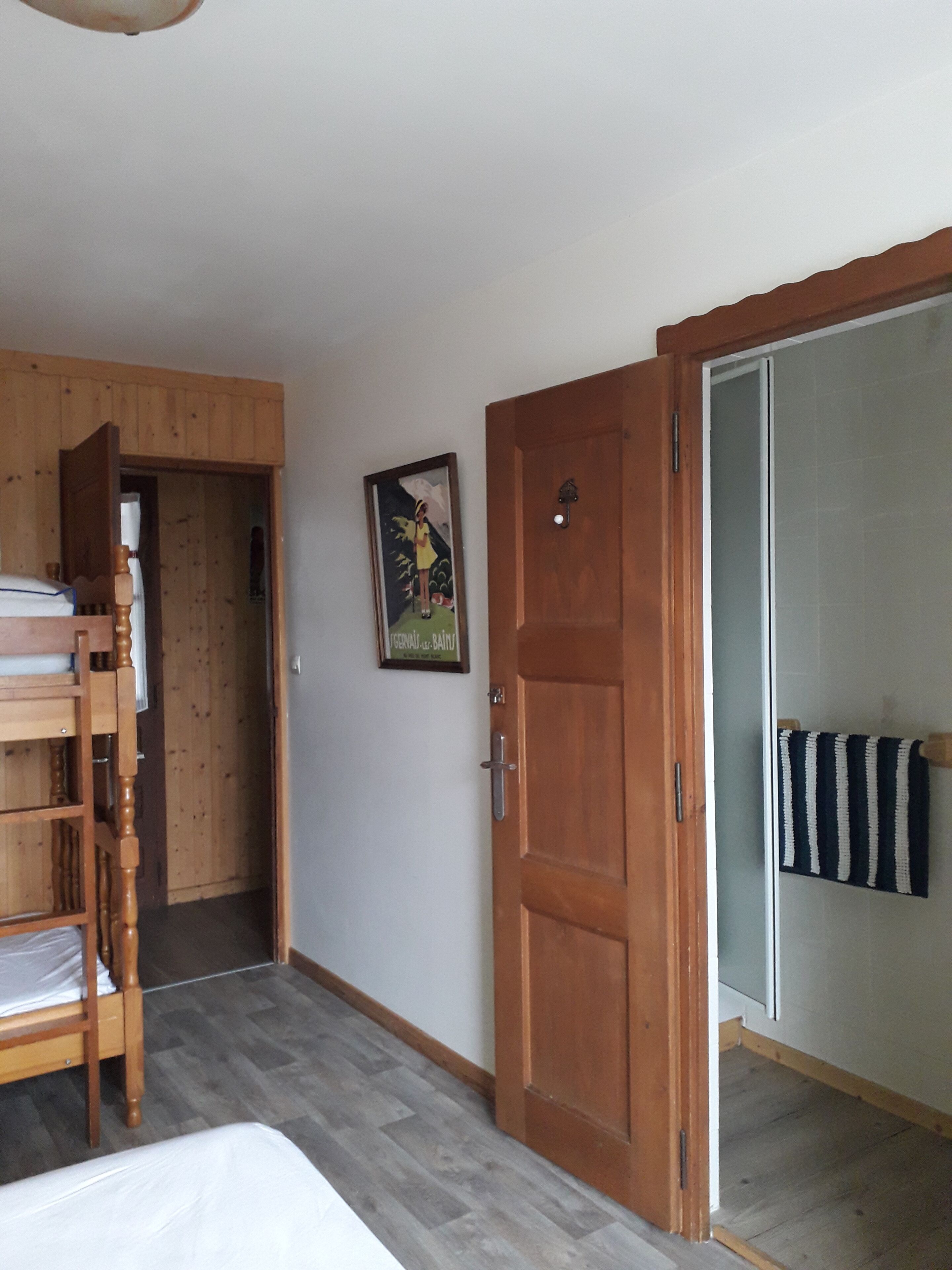 A room with a wooden bunk bed, a door, and a framed picture on the wall.