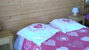 Puupaneelilla verhoiltu huone, jossa on kaksi sänkyä. Jokaisessa sängyssä on sydänkuviollinen päiväpeite, ja huoneessa on yöpöytä lampun kanssa sekä seinälle ripustettu sydänaiheinen taideteos.
