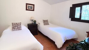 A room with two single beds, a small table with a lamp, a framed picture on the wall, and a window with shutters. - Pretty Reformed Stables With Spectacular Country Views, Private Pool And Gardens (El Tropezon, Colmenar)